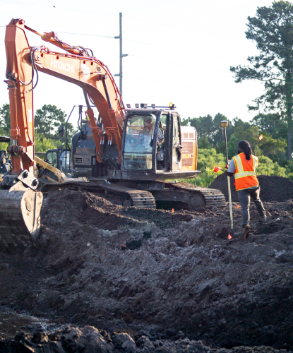 excavator digging trench with workers visible