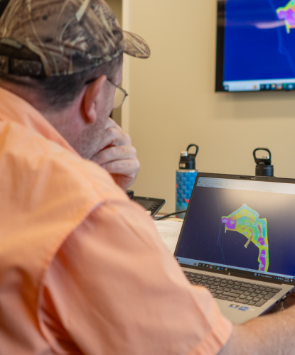 Man in orange shirt views colorful map on computer screen.
