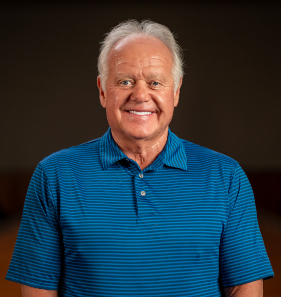 Smiling man in blue striped polo, dark background.