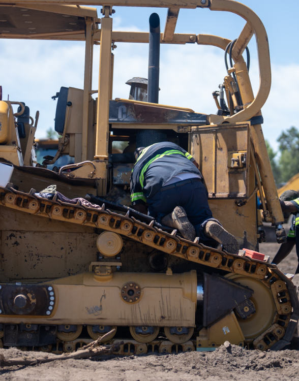 Worker in safety gear examines bulldozer engine at site.