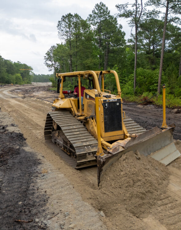 Yellow bulldozer pushes dirt at tree-lined construction site.
