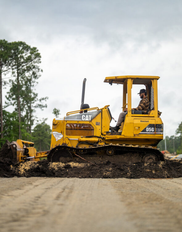 Person drives yellow bulldozer, moving soil on dirt road.