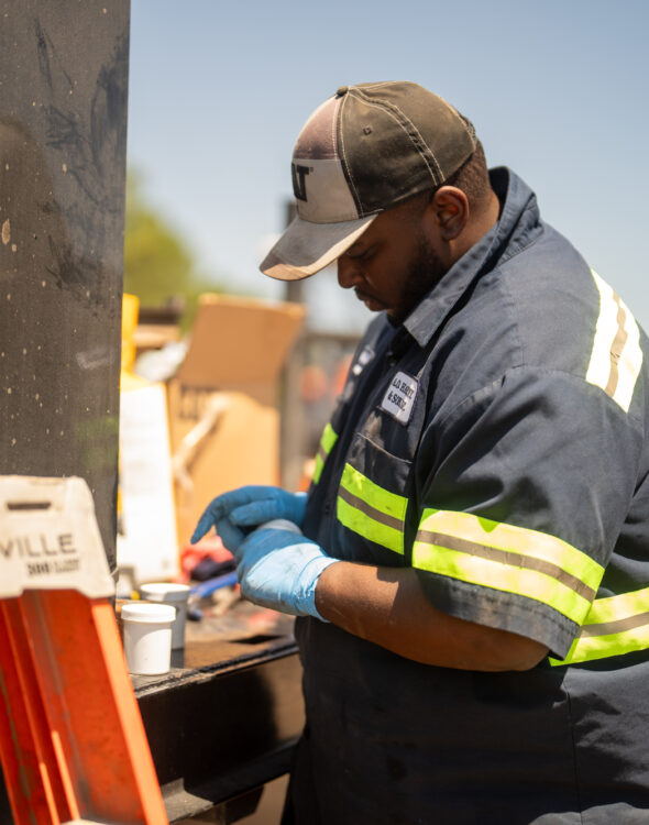 Worker in reflective gear prepares materials at outdoor site.