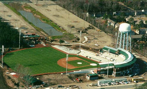 Aerial view: baseball stadium, green field, empty stands, water tower.