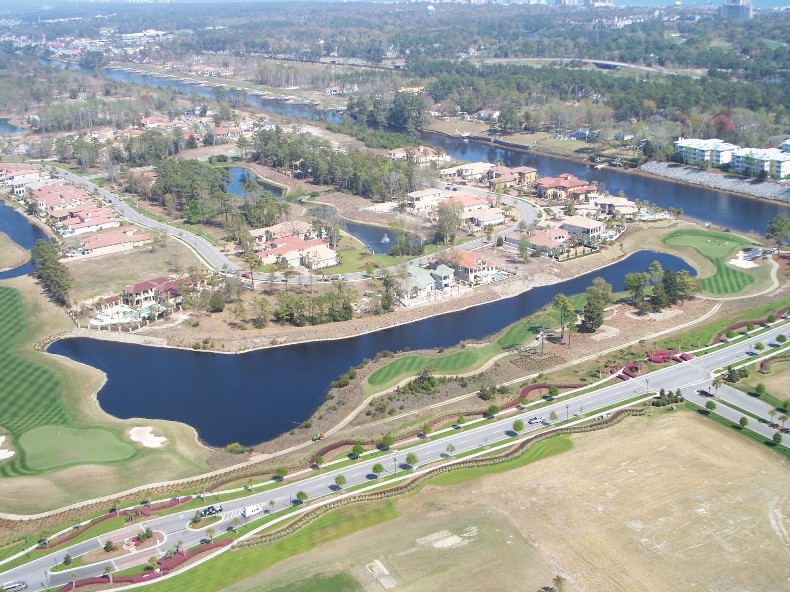 Aerial view of homes, golf course, water, roads, greenery.