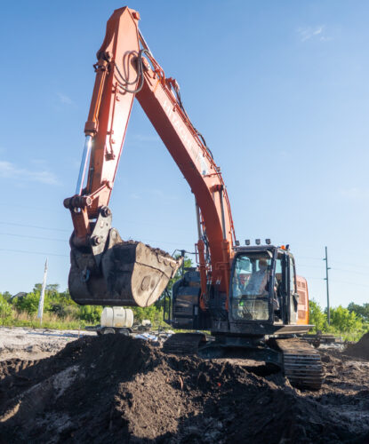 Orange excavator moves dirt at construction site under blue sky.