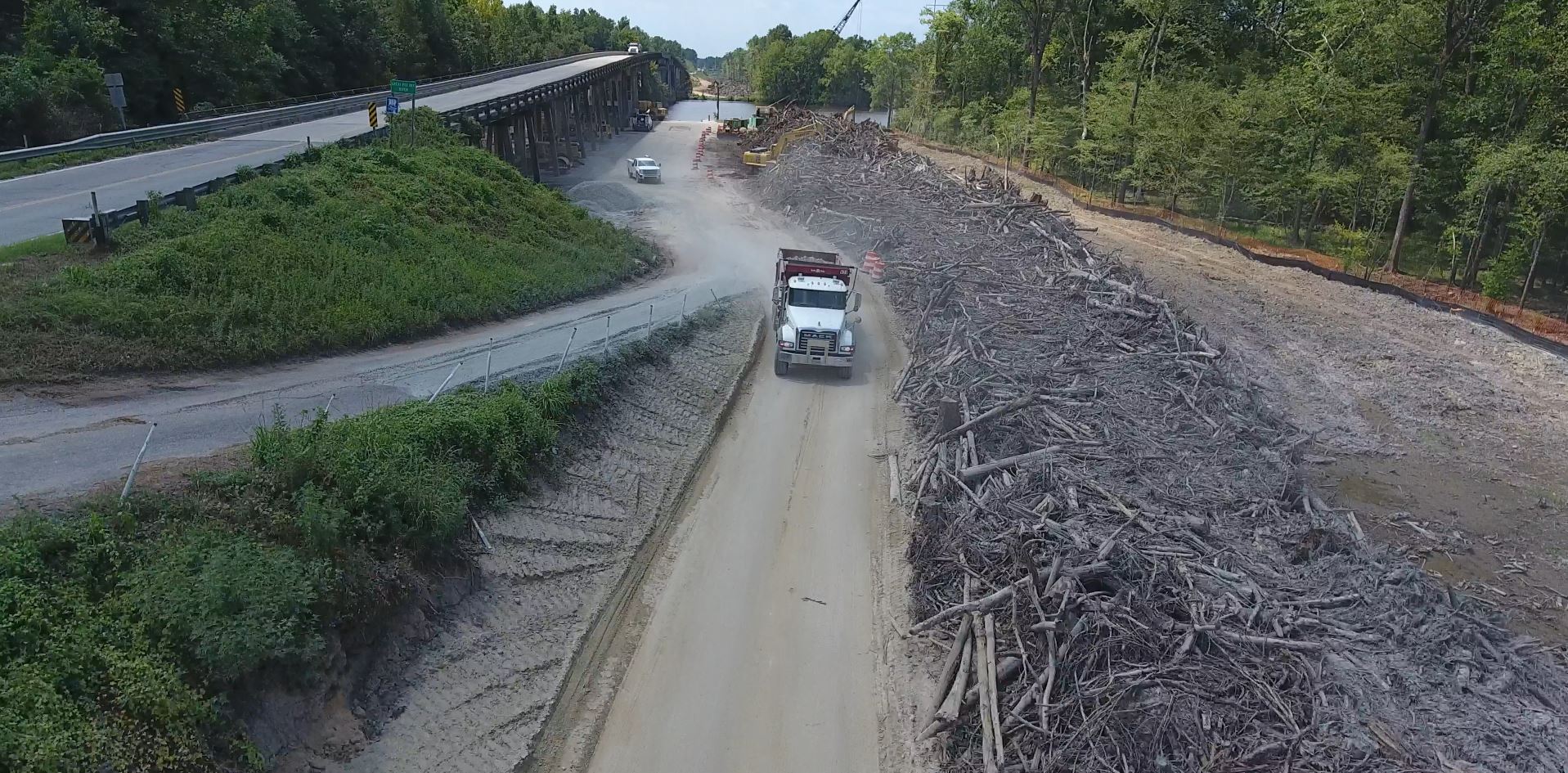 Dump truck drives past tree debris near overpass and woods.