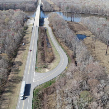 Aerial view: highway, bridge, sparse trees, vehicles, late fall.
