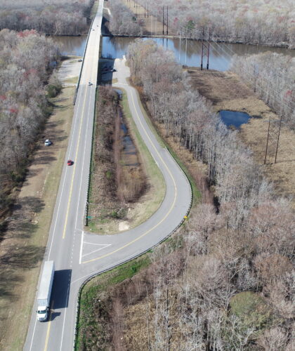 Aerial view: highway, bridge, sparse trees, vehicles, late fall.
