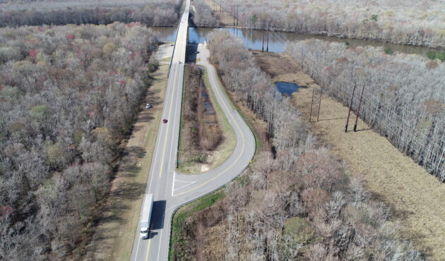 Aerial view: highway, bridge, sparse trees, vehicles, late fall.