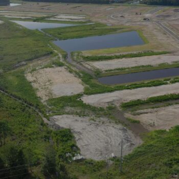Aerial view: construction site, water ponds, dirt roads, forest.