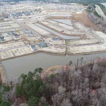 Aerial view: housing development under construction with roads, ponds, woods.