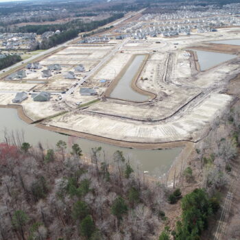 Aerial view: houses under construction, cleared lots, forest, road.