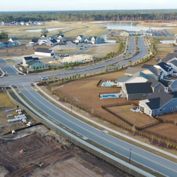 Aerial view of suburban homes, roads, construction, and pond.