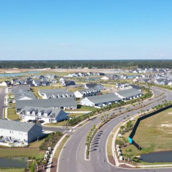 Aerial view: suburban houses, curved streets, ponds, green spaces.