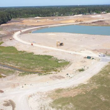 Aerial view: construction site, earthmovers, water, dirt roads, vegetation.