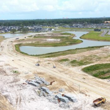 Aerial view: construction site, dirt roads, materials, neighborhood, pond.