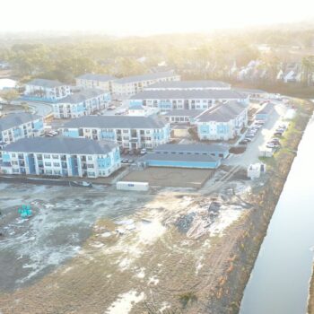 Aerial view: housing complex construction beside canal, roads, houses.