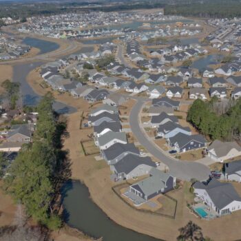 Aerial view of suburban homes, curved streets, ponds, trees.