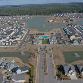 Aerial view: suburb, homes, roads, ponds, central pool area.