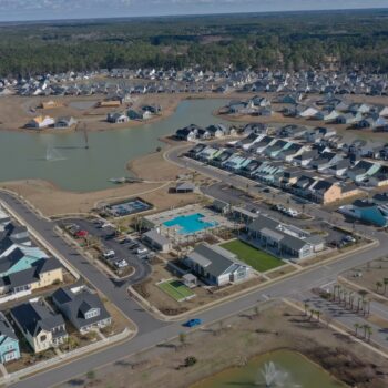 Aerial view: suburb with houses, lakes, pool, woods nearby.
