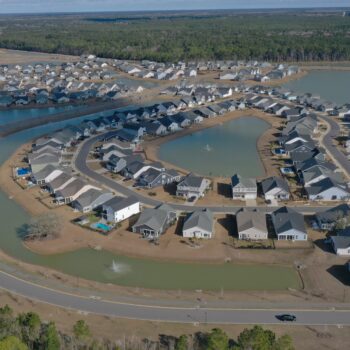 Aerial view: suburban homes, winding streets, ponds, wooded areas.