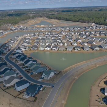 Aerial of suburban homes, curved streets, ponds, and sparse trees.