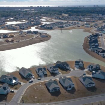 Aerial view: houses encircle a large pond and curving roads.