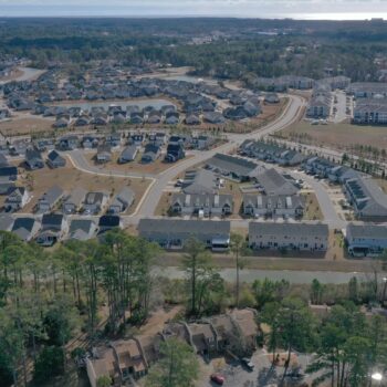 Aerial view of suburb: houses, pond, roads, trees, apartments.