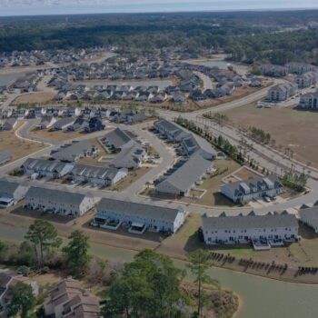Aerial view of suburban homes, roads, water, and trees.