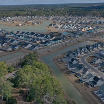 Aerial view of houses, canals, and trees beneath clouds.