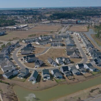 Aerial view of round suburb, roads, water, open land.