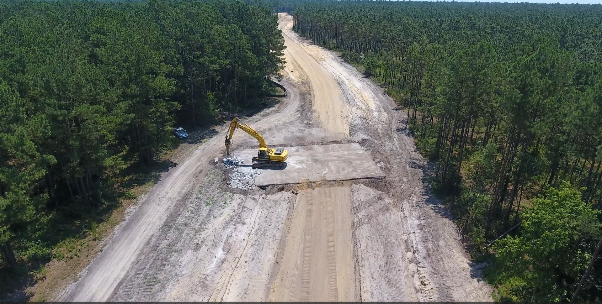 Yellow excavator works on dirt road by dense forest.