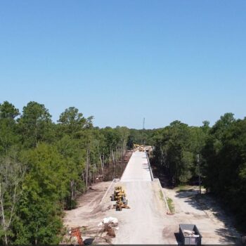 Construction machines building road through forest under blue sky.