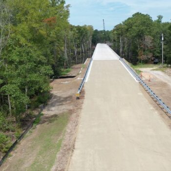 Partially built bridge, dirt road, trees, construction vehicles right.