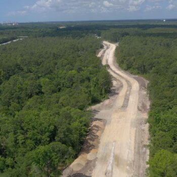 Aerial view: dirt road cuts through forest under cloudy sky.