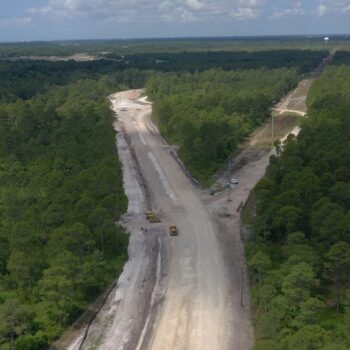 Aerial view: construction vehicles clearing a dirt road through forest.