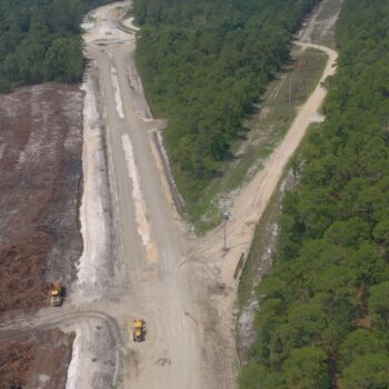 Aerial view: construction site, dirt roads, vehicles, surrounding trees.