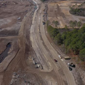 Aerial view of construction site with road, trees, vehicles.