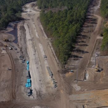 Aerial view: construction site, equipment, materials, and surrounding forest.