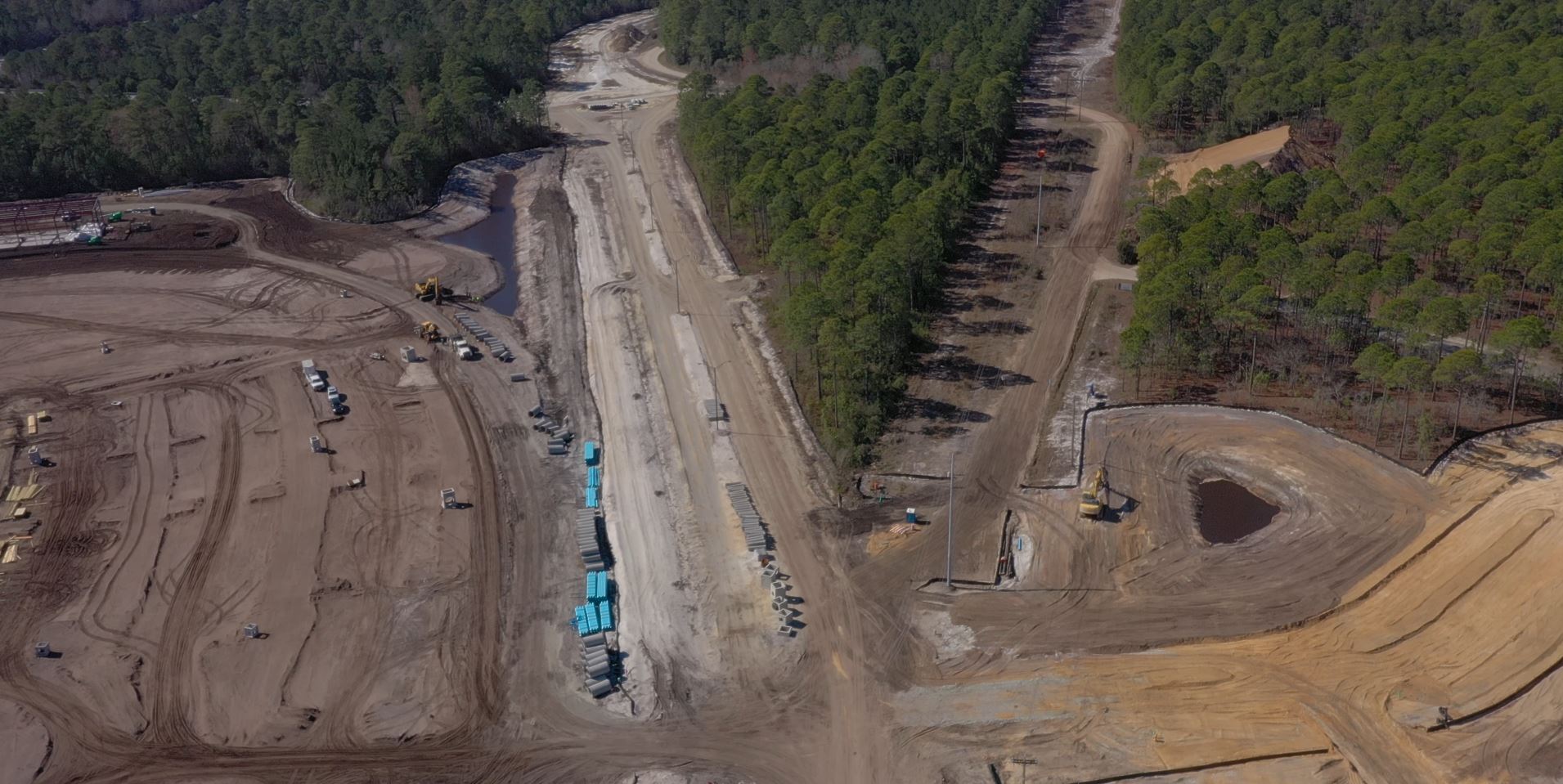 Aerial view: construction site, vehicles, materials, and forest nearby.