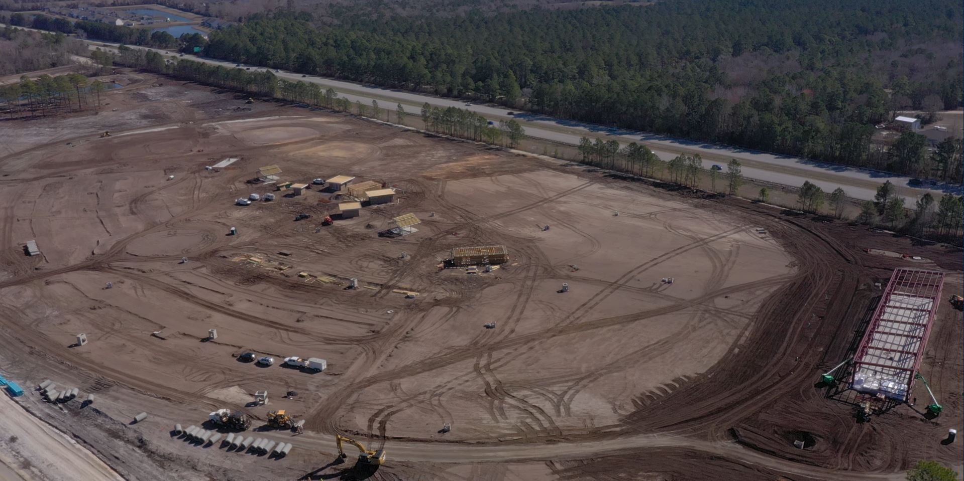 Aerial view: construction site, equipment, materials, dirt, road, forest.