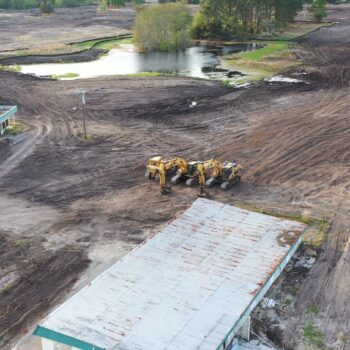 Aerial view: construction site, machinery, pond, two large buildings.