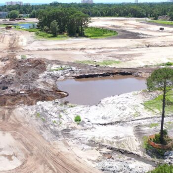 Aerial view: construction site, dirt roads, pond, tree with barrier.