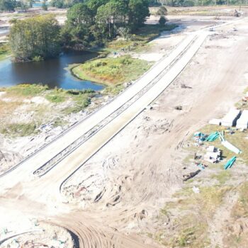 Aerial view: construction site, unfinished roads, machinery, pond, trees.