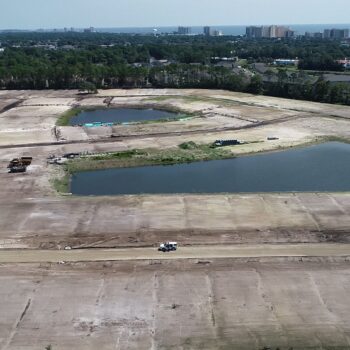 Aerial view: construction site, two ponds, vehicles, homes, high-rises.