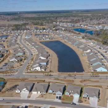 Aerial view: houses, roads, pond, and greenery in suburb.