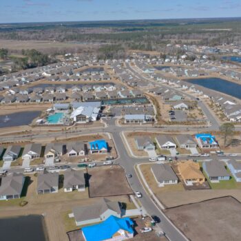 Aerial view: suburban homes, pools, ponds, empty lots.