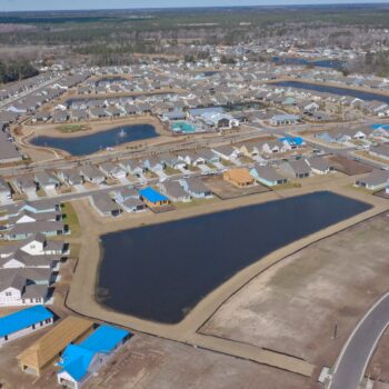 Aerial view: suburban homes, lakes, constructions, roads, woods.