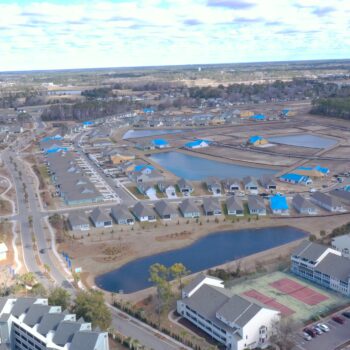 Suburban aerial view: houses, ponds, tennis courts, blue-roof construction.